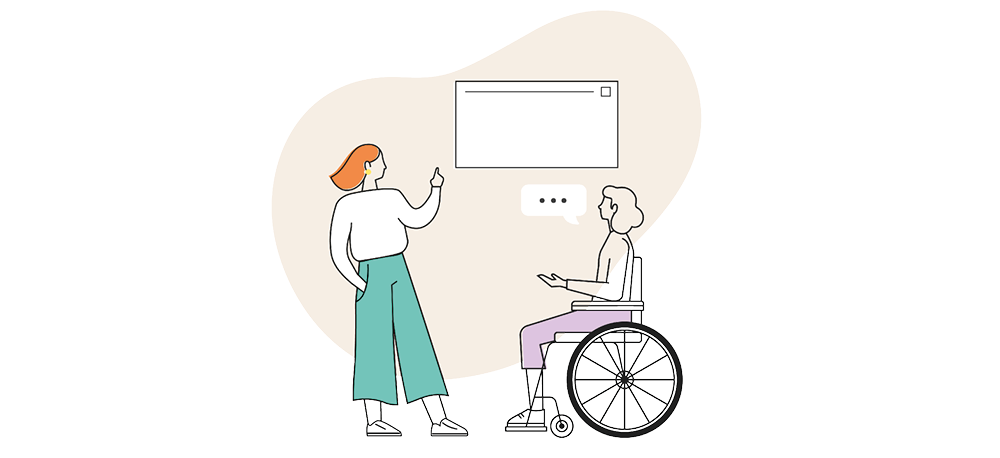 Two women talking. One is stood up pointing at a whiteboard. The other is in a wheelchair.