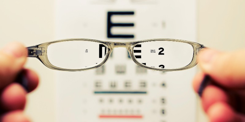 View through a pair of glasses being held in front of an opticians eye chart.